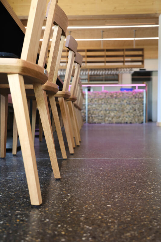 Terrazzo-Bodenbelag in einem Restaurant, mit Stuhlbeinen aus hellem Holz im Vordergrund.
