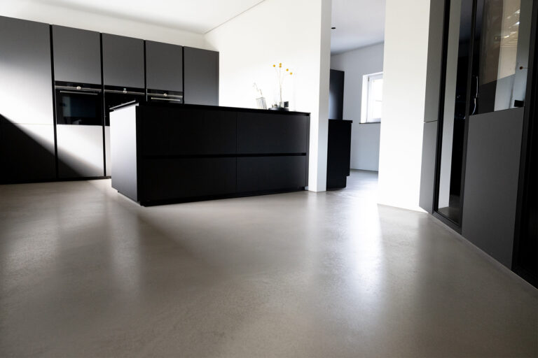 Moderner, fugenloser Boden in einer minimalistischen Küche mit schwarzen Schränken und Kücheninsel.