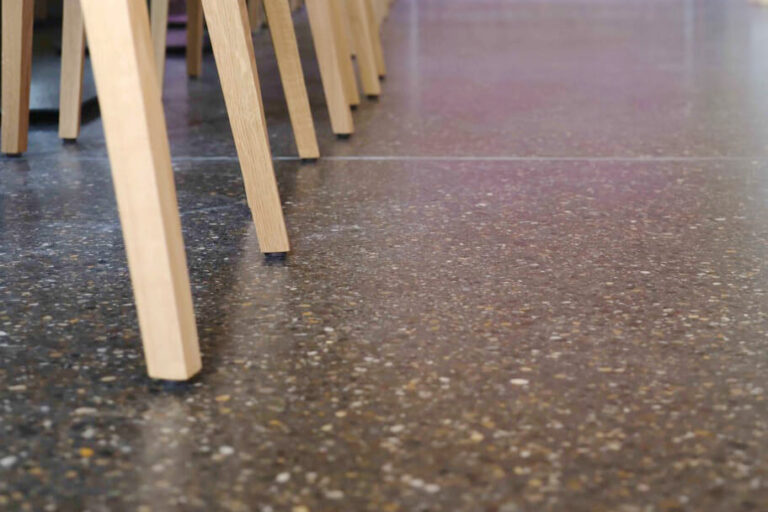 Terrazzo-Bodenbelag in einem Restaurant, mit Stuhlbeinen aus hellem Holz im Vordergrund.